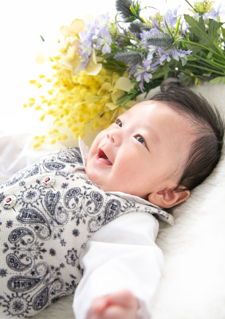 お宮参り：ベビードレスを着てお花と一緒に微笑む男の子の赤ちゃん