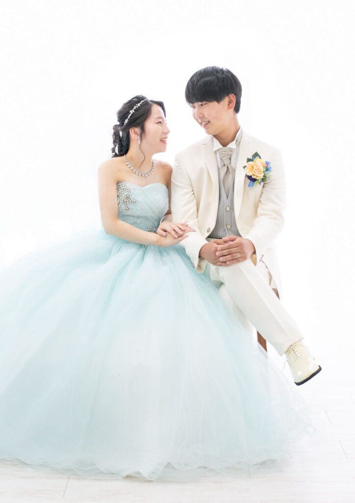 ウェディング：パステルブルーのドレスを着た新婦と白いタキシードを着た新郎が並んで座り、見つめ合う様子