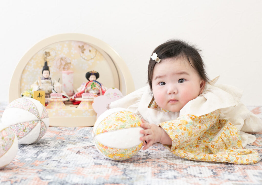 お節句：フリル付き着物を着て手毬で遊ぶ女の子の赤ちゃん