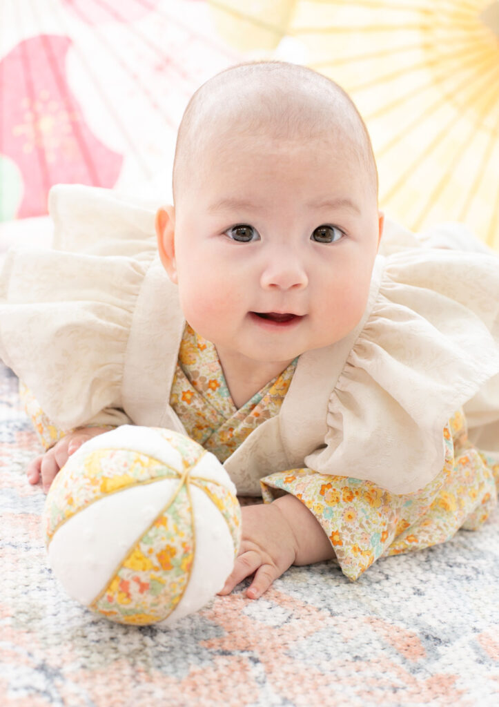 お節句：フリル付き着物を着て手毬と遊ぶ女の子の赤ちゃん