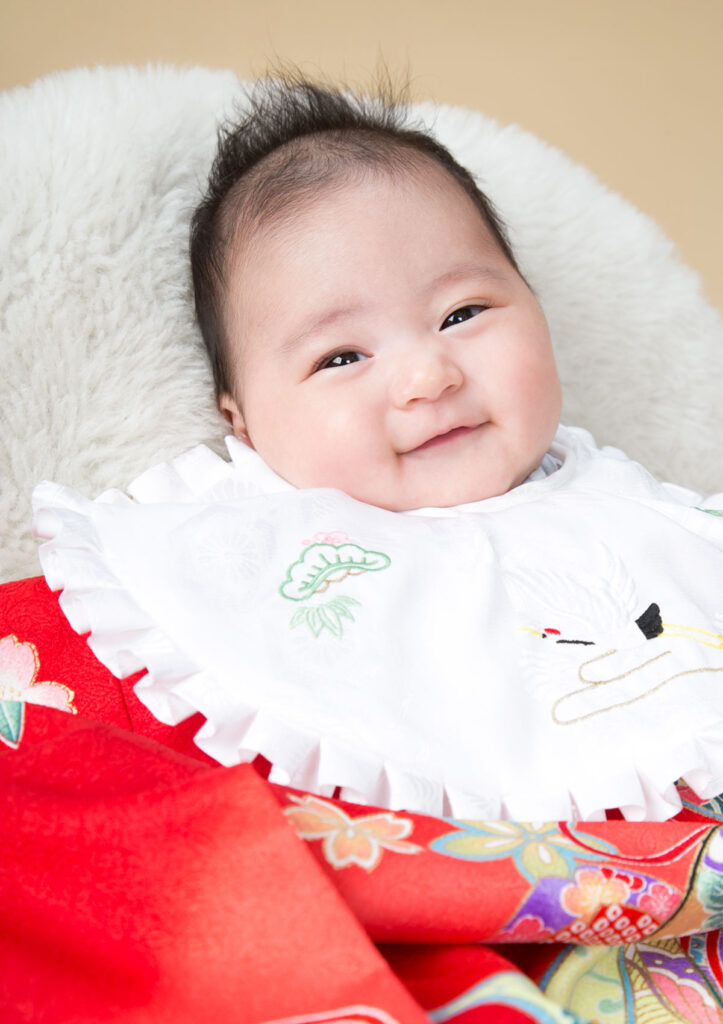 お宮参り：赤い産着を着て優しく微笑む女の子の赤ちゃん