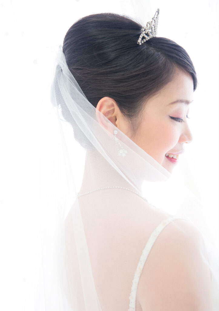 ウェディング：白いベール越しに優しく微笑んだ横顔を見せる新婦