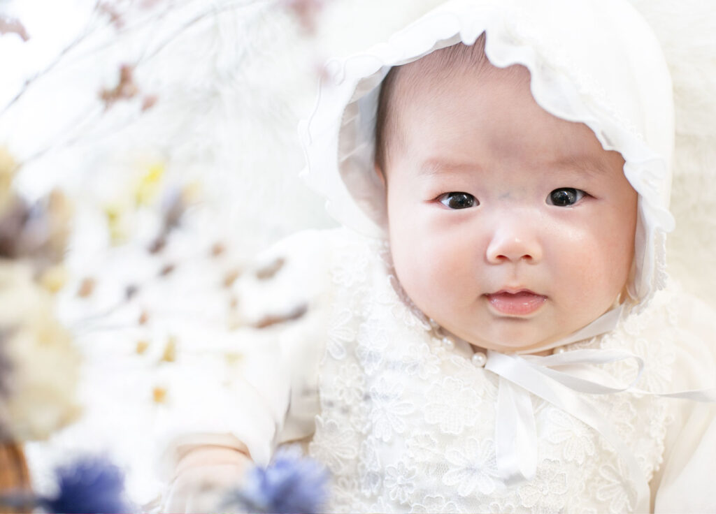 お宮参り：白いベビードレスを着てカメラを見つめる女の子の赤ちゃん