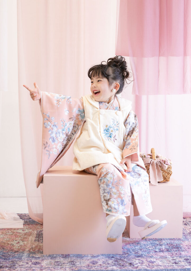 U2024-3model_753 七五三:くすみピンクの花柄の着物にアイボリーの被布を合わせてた着物を着て、楽しそうに指をさす3歳の女の子