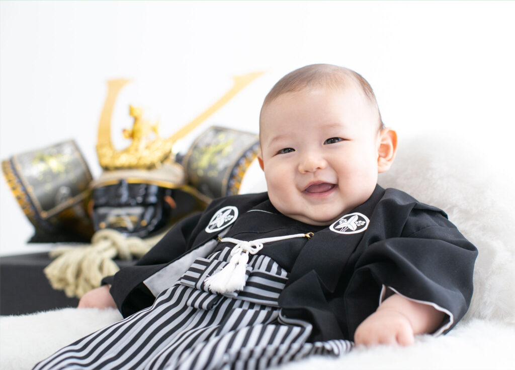 お節句：兜人形を背景に黒い着物を着て笑う男の子の赤ちゃん