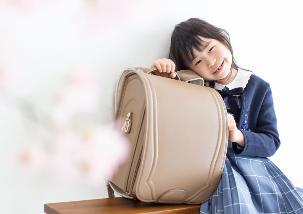 入学：おしゃれなキャメルカラーのランドセルに寄りかかって微笑む女の子