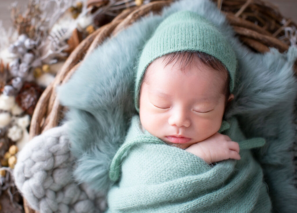 ニューボーン：ドライフラワーに囲まれた籠の中で、くすみグリーンのおくるみにくるまれて眠る赤ちゃん