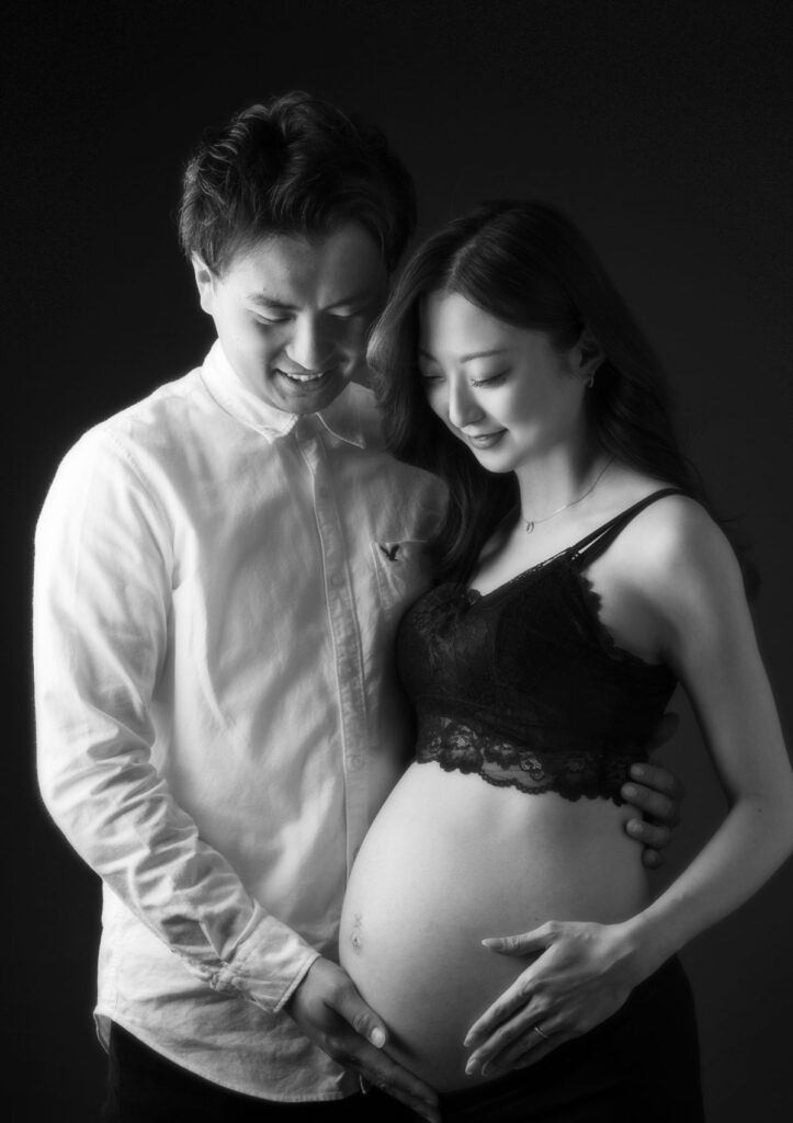 マタニティ：赤ちゃんがいるお腹をパパとママが寄り添い優しく見つめるモノクロフォト