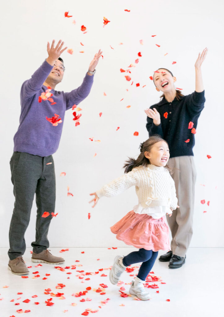 ファミリー：空中に沢山舞う花びらの中を楽し気に駆け回る女の子と両親