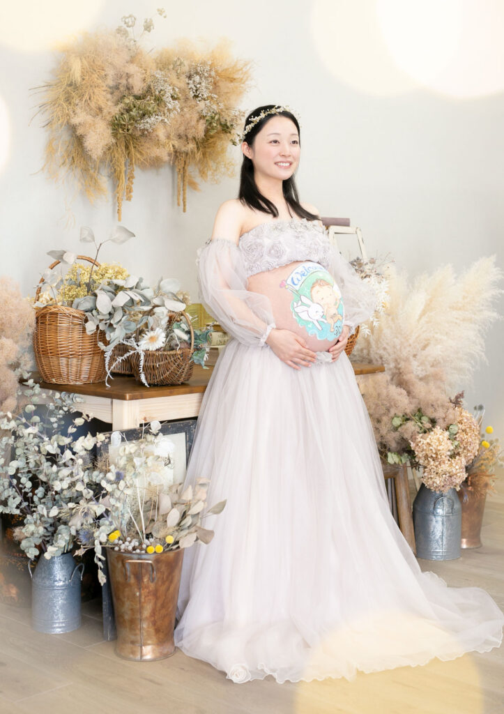 マタニティ：グレージュのマタニティドレスを着てドライフラワーのセットでたたずむママ