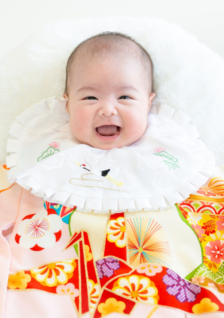 お宮参り：ピンクの産着を着てお口を開けて笑う女の子の赤ちゃん