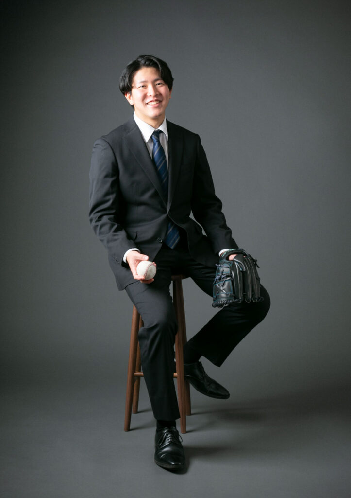 成人式：成人の記念にスーツを着用して、野球ボールとグローブと共に笑顔で椅子に腰かける男性