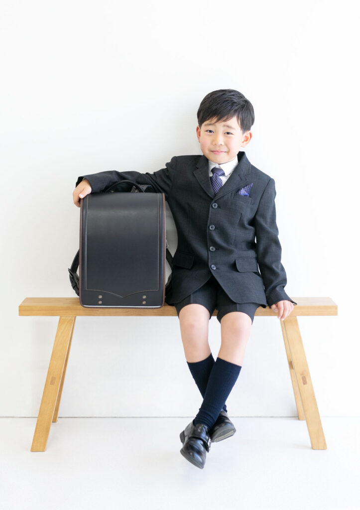 入学：知的な雰囲気でベンチにランドセルと共に座る男の子