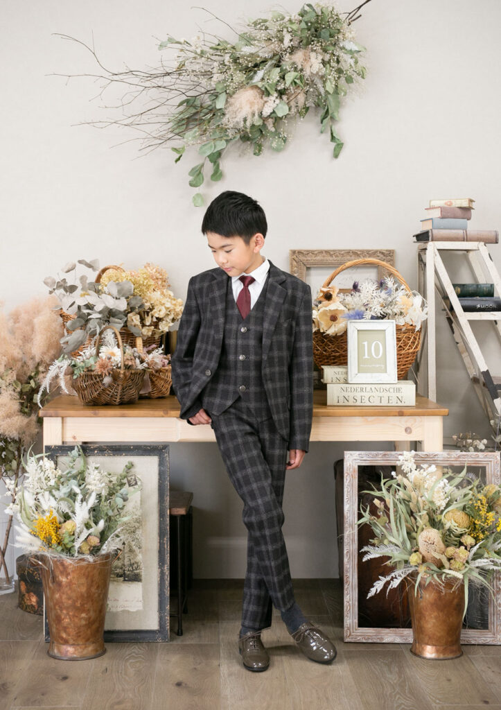 ハーフ成人：スラリとした足を交差させて、スーツで大人っぽくポーズをとる10才の男の子
