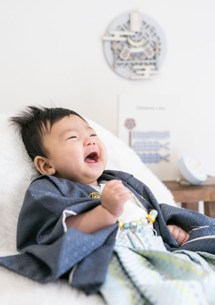 お節句：兜や鯉のぼりのデザインパネルを背に着物を着て笑う男の子の赤ちゃん