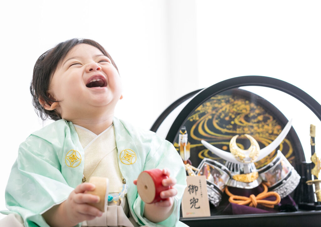 お節句：着物を着て兜人形と並んで笑う男の子の赤ちゃん