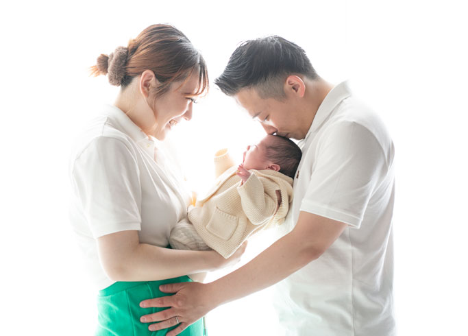 ニューボーン：パパとママに優しく抱えられ、パパから額にキスをしてもらう赤ちゃん