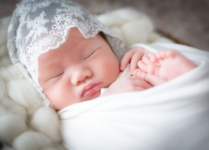 ニューボーン：白いおくるみに包まれレースの帽子をかぶって眠る赤ちゃん