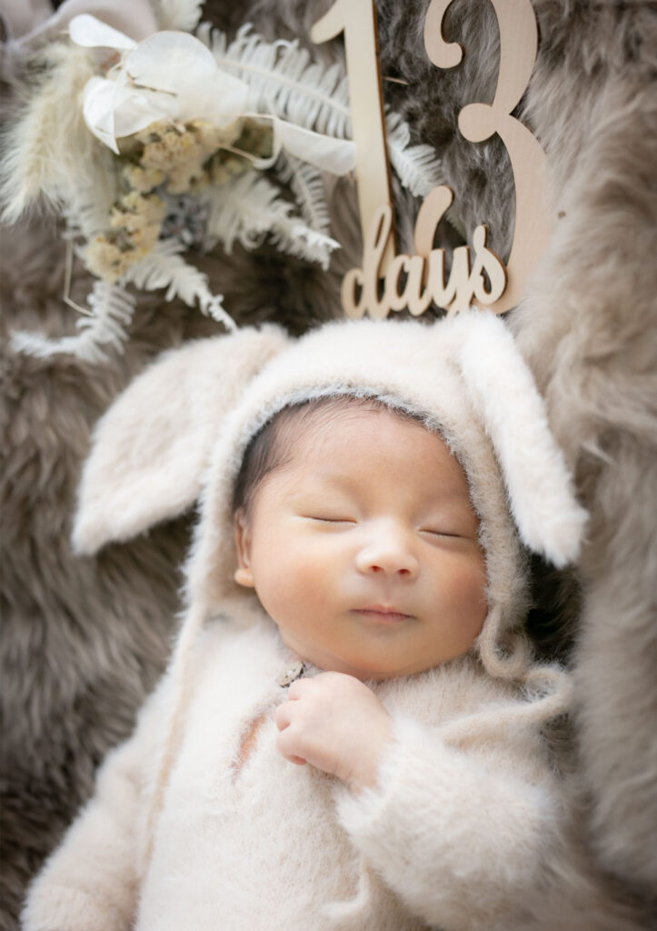 ニューボーン：ふわふわのロンパースにうさ耳付き帽子をかぶって眠る赤ちゃん