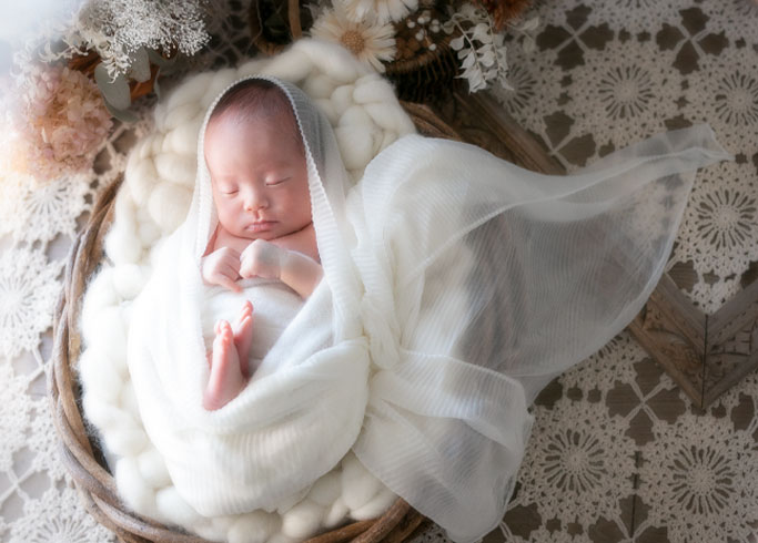 ニューボーン：天使の羽のようにあしらわれた白いおくるみに包まれ眠る赤ちゃん