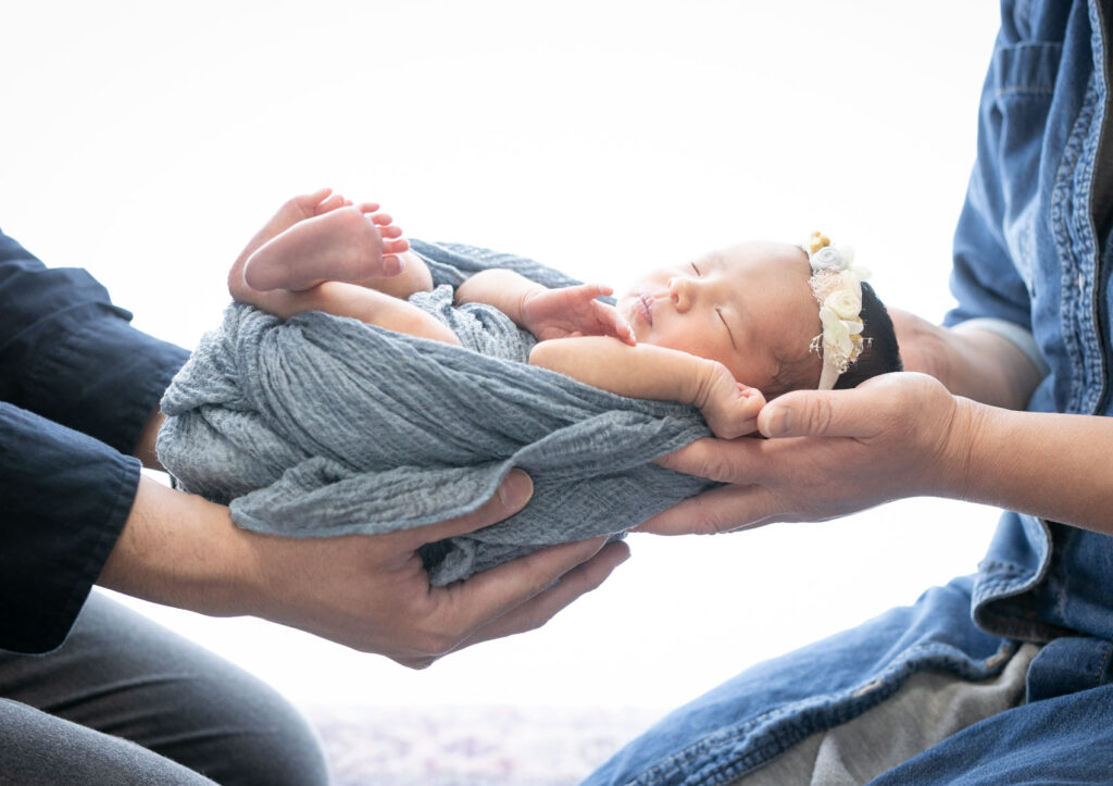 ニューボーン：ブルーのおくるみに包まれてパパとママの手のひらで抱えられた赤ちゃん