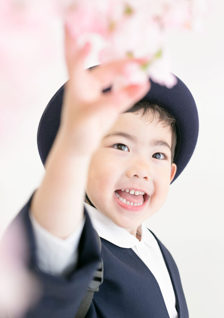 入園：桜の花を手に取って、大きく口を開けて笑う男の子