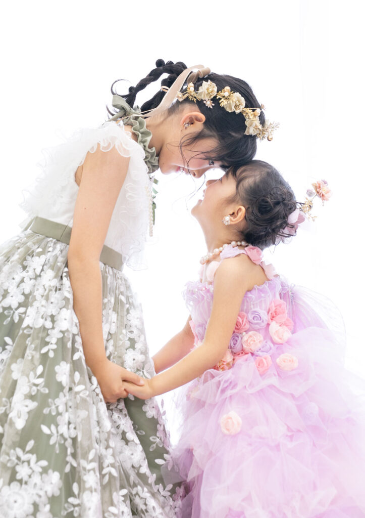 家族衣装：手を繋いでおでこ同士をくっつけて笑い合う、ドレスを着た姉妹