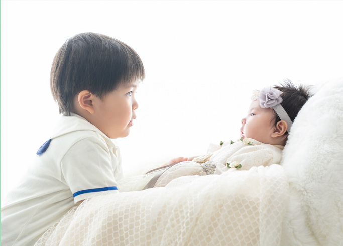 お宮参り：ベビードレスを着てお兄ちゃんと見つめ合う赤ちゃん