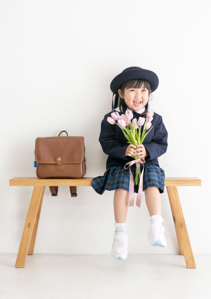 入園：楽しそうに笑いながら、両手でチューリップをもってベンチに座る女の子