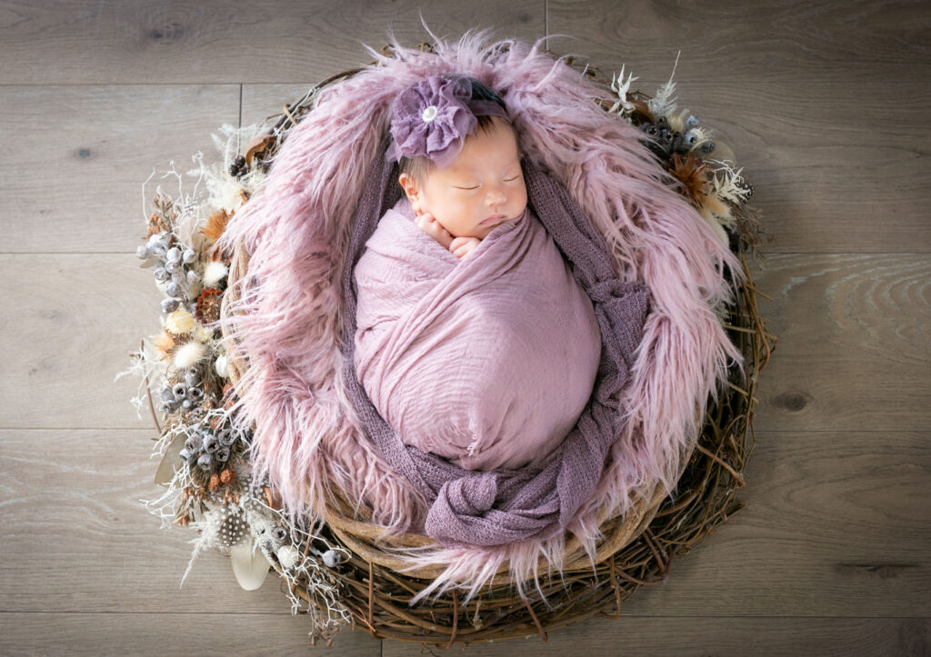ニューボーン：ドライフラワーで飾られたかごの中でパープルのおくるみに包まれて眠る赤ちゃん