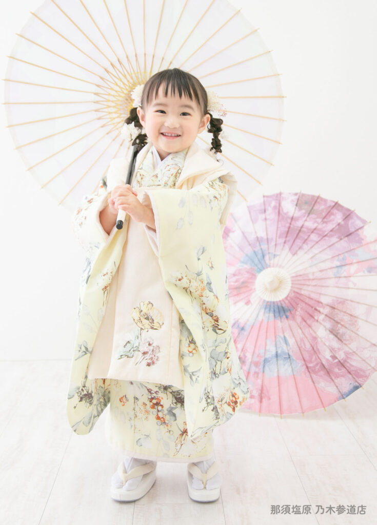 七五三３歳着物：トレンドのボタニカル柄のクリーム色の着物を着た3歳の女の子。