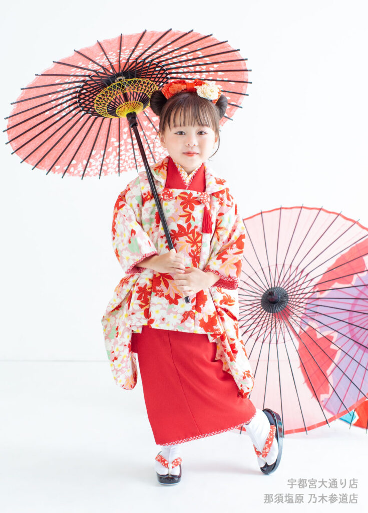 五三３歳着物：もみじ柄の赤い着物を着て和傘をさす３才の女の子。