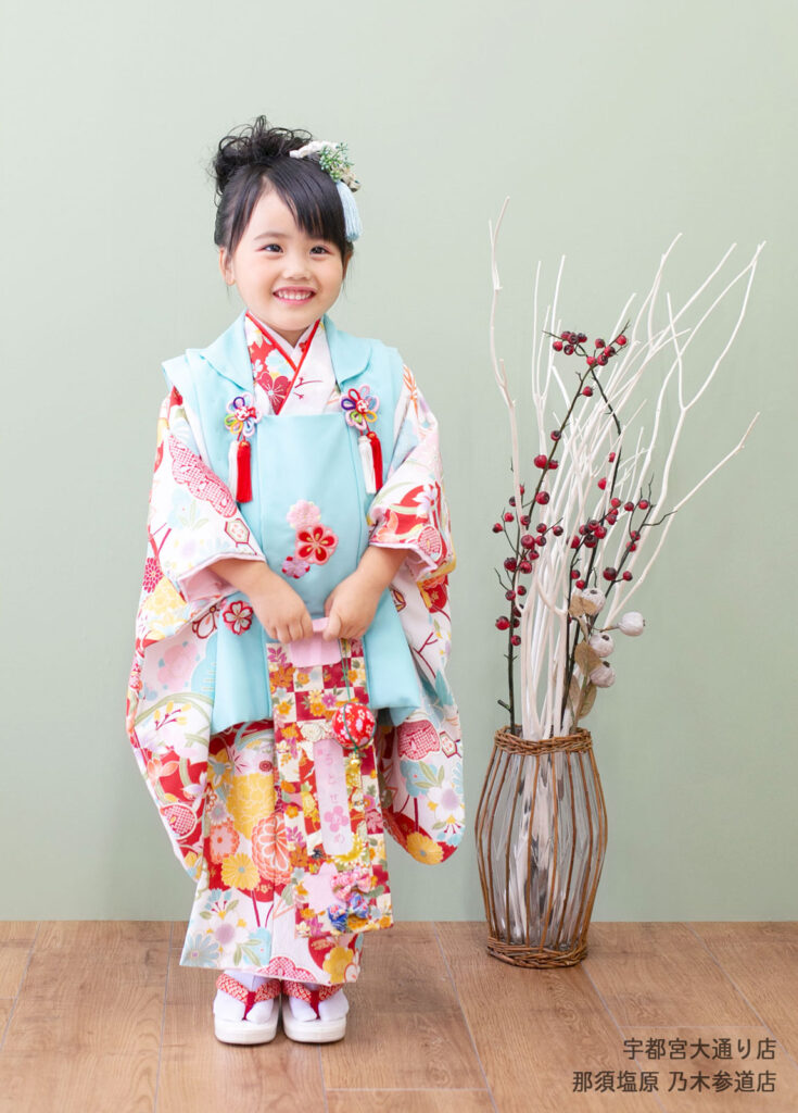 七五三３歳着物：白地に赤い花がちりばめられた着物、水色の被布を合わせた明るいコーディネートの3歳の女の子。