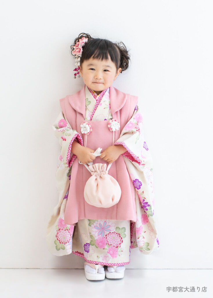 七五三３歳着物：くすんだピンクの被布と渋めのベージュの高級感のある着物を着た３才の女の子。
