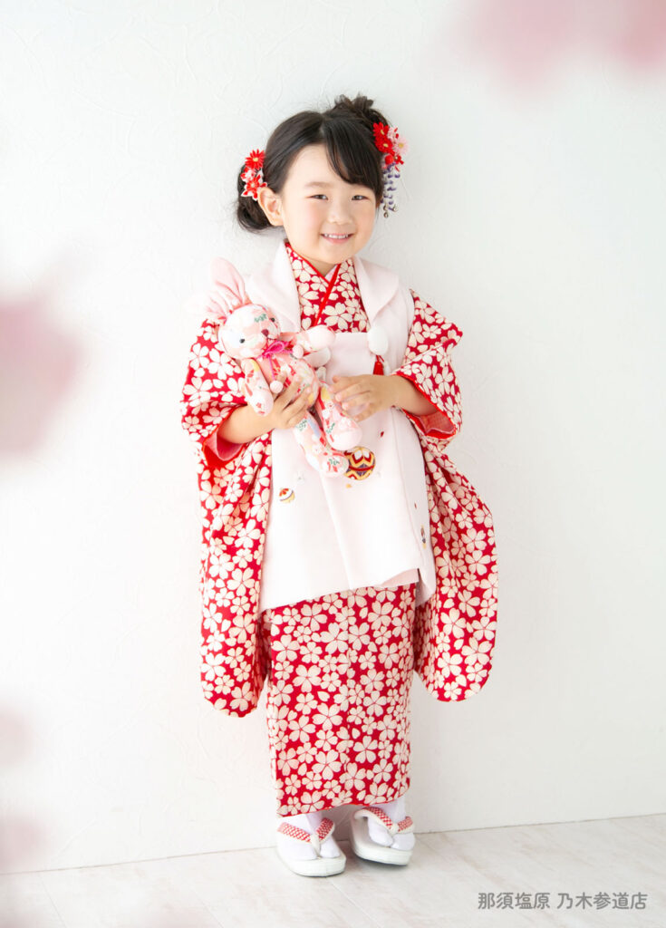 七五三３歳着物：赤い桜模様の着物を着てウサギのぬいぐるみを持つ３才の女の子。