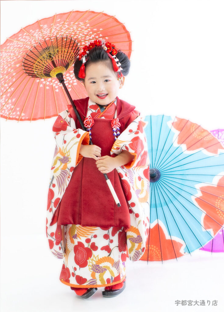 七五三３歳着物：赤い梅柄の着物を着た日本髪の３才の女の子。