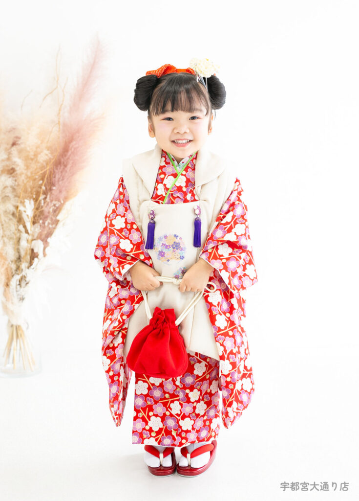 七五三３歳着物：赤い梅の花柄に白い被布を合わせた人気の着物を着た３歳の女の子。
