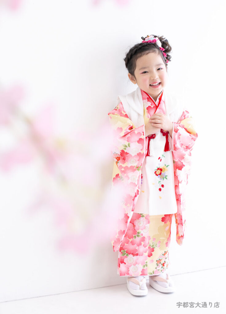 七五三３歳着物：クリーム色にピンクの桜がたくさん描かれた着物を着た３才の女の子。