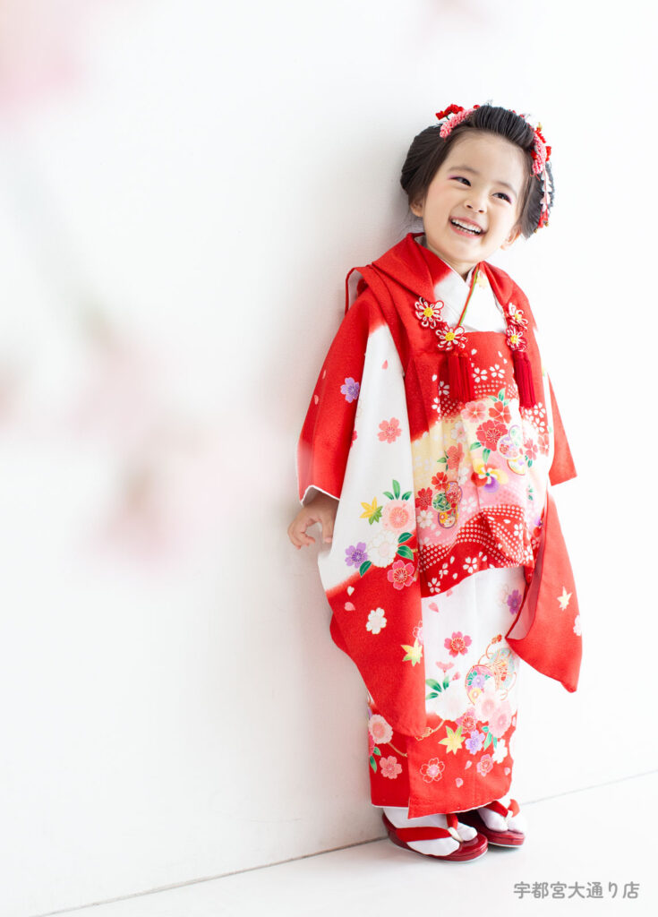 七五三３歳着物：赤い古典的な着物を着たかわいい笑顔の日本髪の３才の女の子。