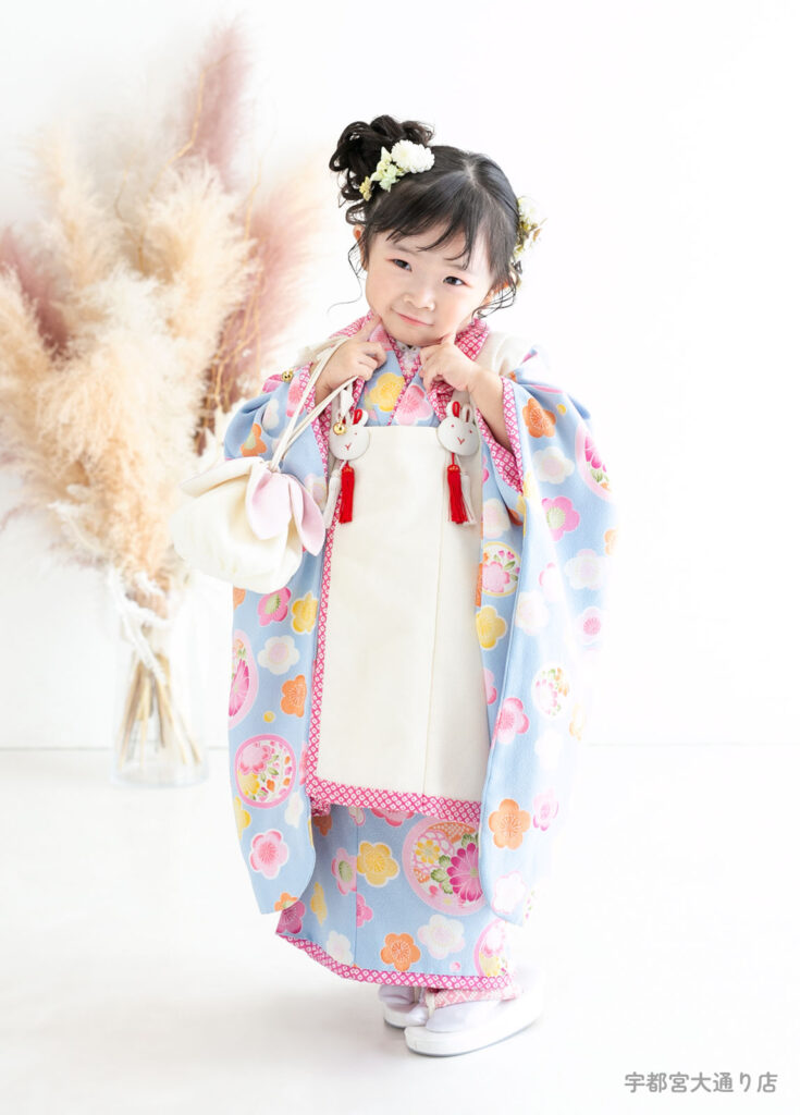 五三３歳着物：水色にウサギの飾りがついた着物をきたかわいいポーズの３才の女の子。