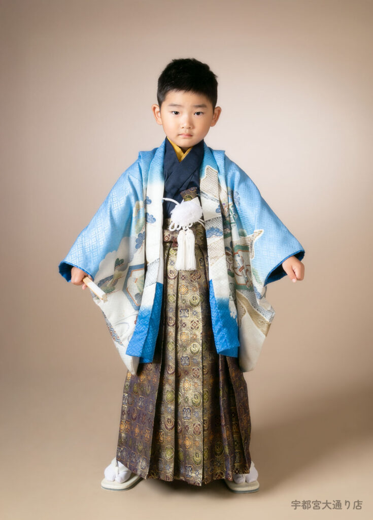 七五三５歳着物：縁起の良い松がたくさん描かれた水色の着物を着た緊張気味の５才の男の子。