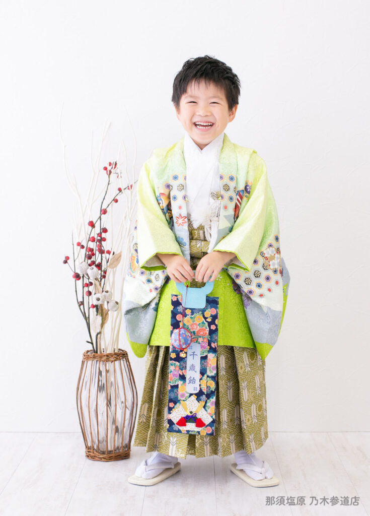 七五三５歳着物：ライムグリーン色の着物を着て千歳あめをもって笑う５才の男の子。