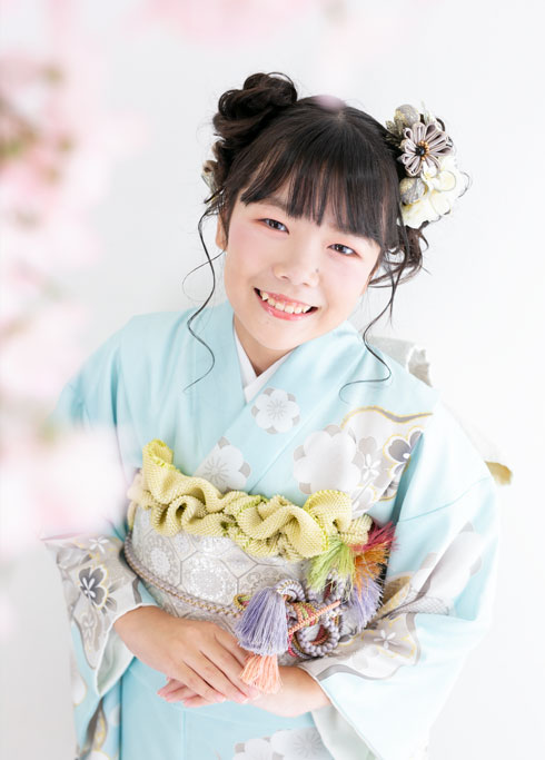 ハーフ成人：桜と一緒に、にこやかに微笑むブルーの着物を着た女の子