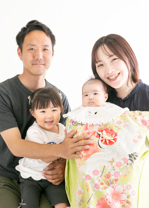 お宮参り：パパとママに抱っこされた、女の子用の産着をきた赤ちゃんとお姉さん