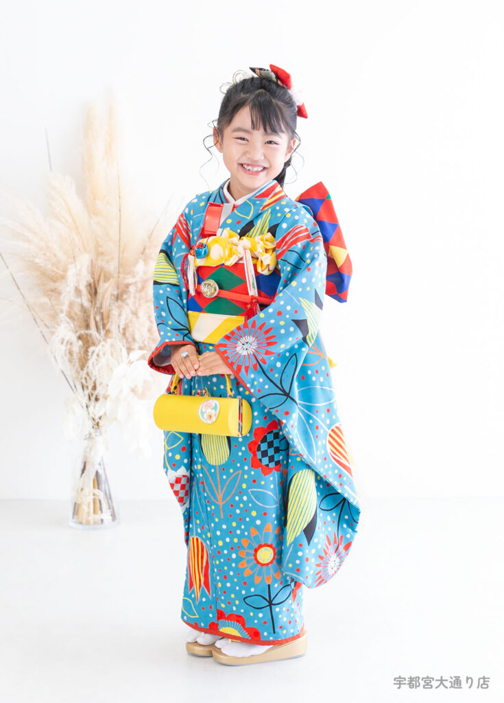 七五三７歳着物：ポップなブルーの着物を着た元気な笑顔の7歳の女の子。個性的な着物はモダンアンテナのもの。