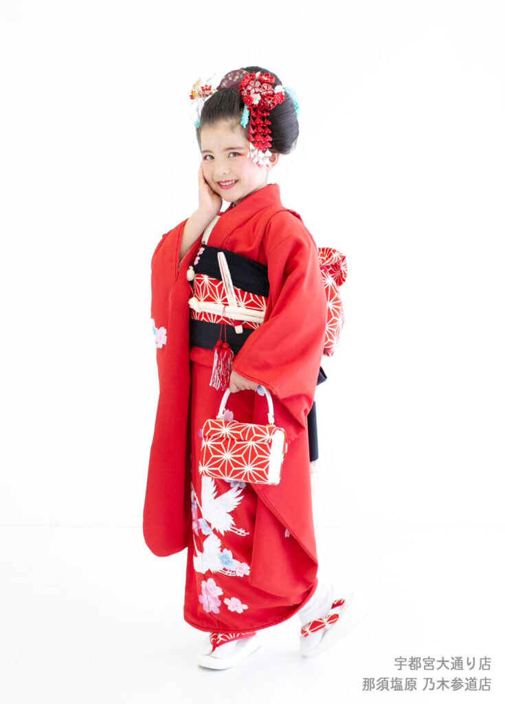 七五三７歳着物：鶴の刺繍が施された真っ赤な着物を着て笑う７才の女の子。