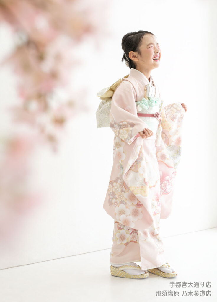 七五三７歳着物：あわい桃色の日本的な着物の袖を広げて笑う７才の女の子。