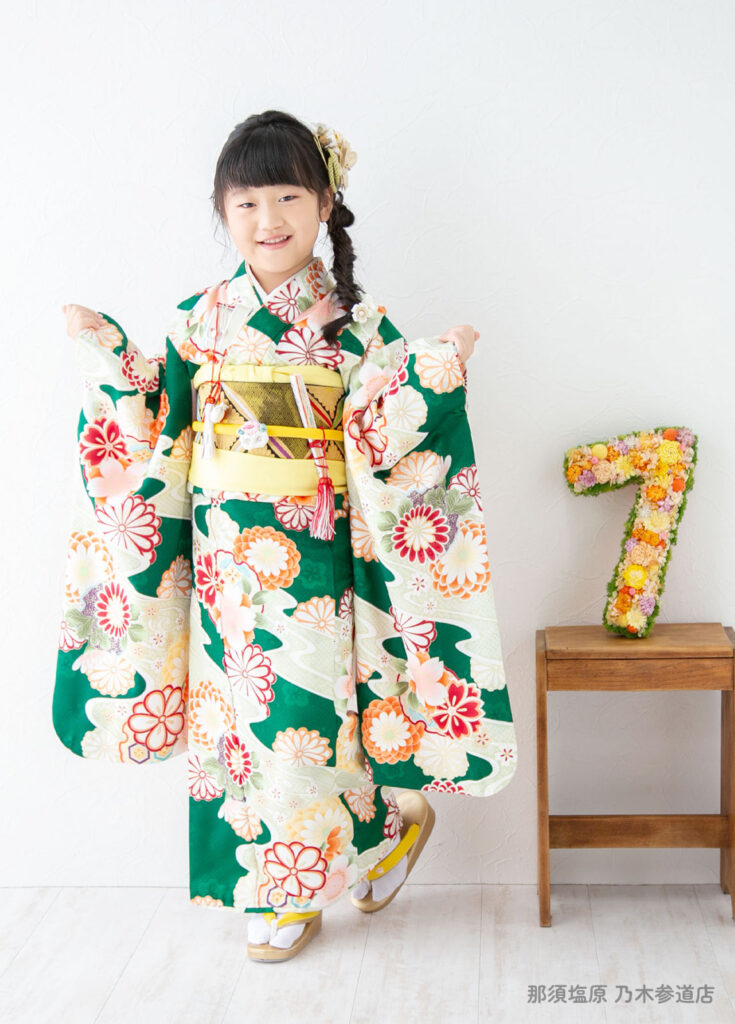 七五三７歳着物：グリーンにオレンジの花がちりばめられた豪華な着物を着た７才の女の子。