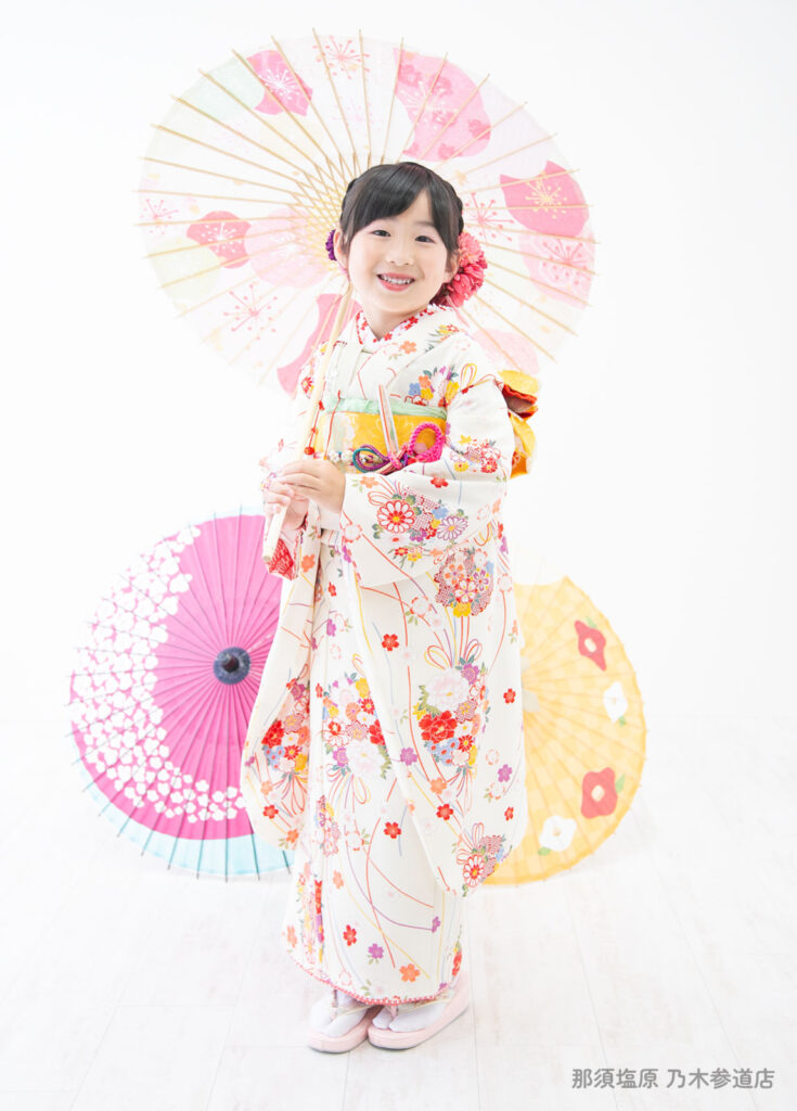 七五三７歳：白い着物を着て和傘をもって微笑む７才の女の子。