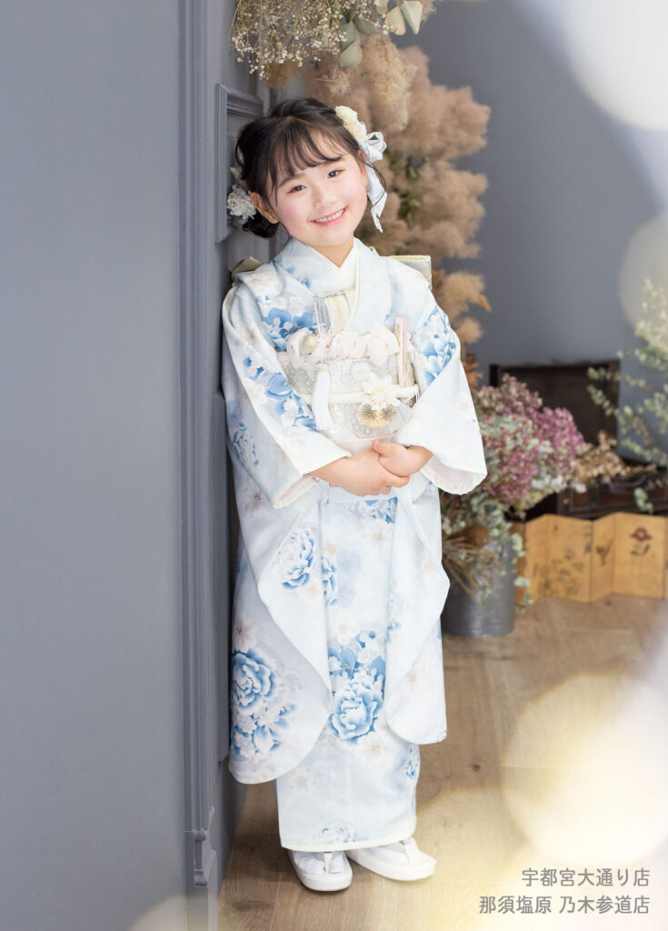 七五三７歳着物：薄いブルーの洋風花柄の着物を着た、髪にたくさんリボンを飾った女の子。
